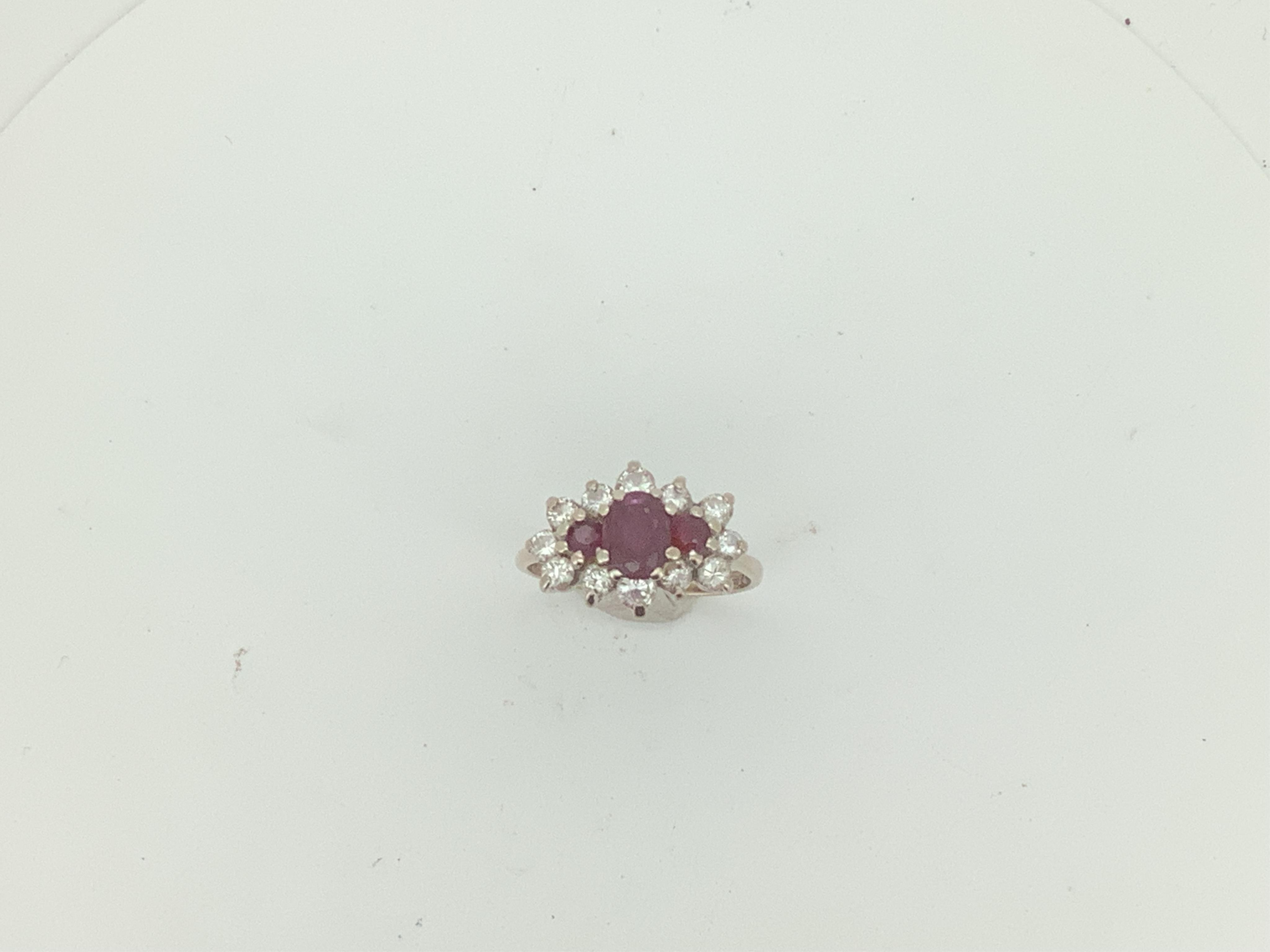 A ruby and diamond ring, set with an oval ruby between two circular-cut rubies, within an outer border of brilliant-cut diamonds totalling approximately 0.65 carats, mounted in 18ct white gold, size O, British hallmarks,
